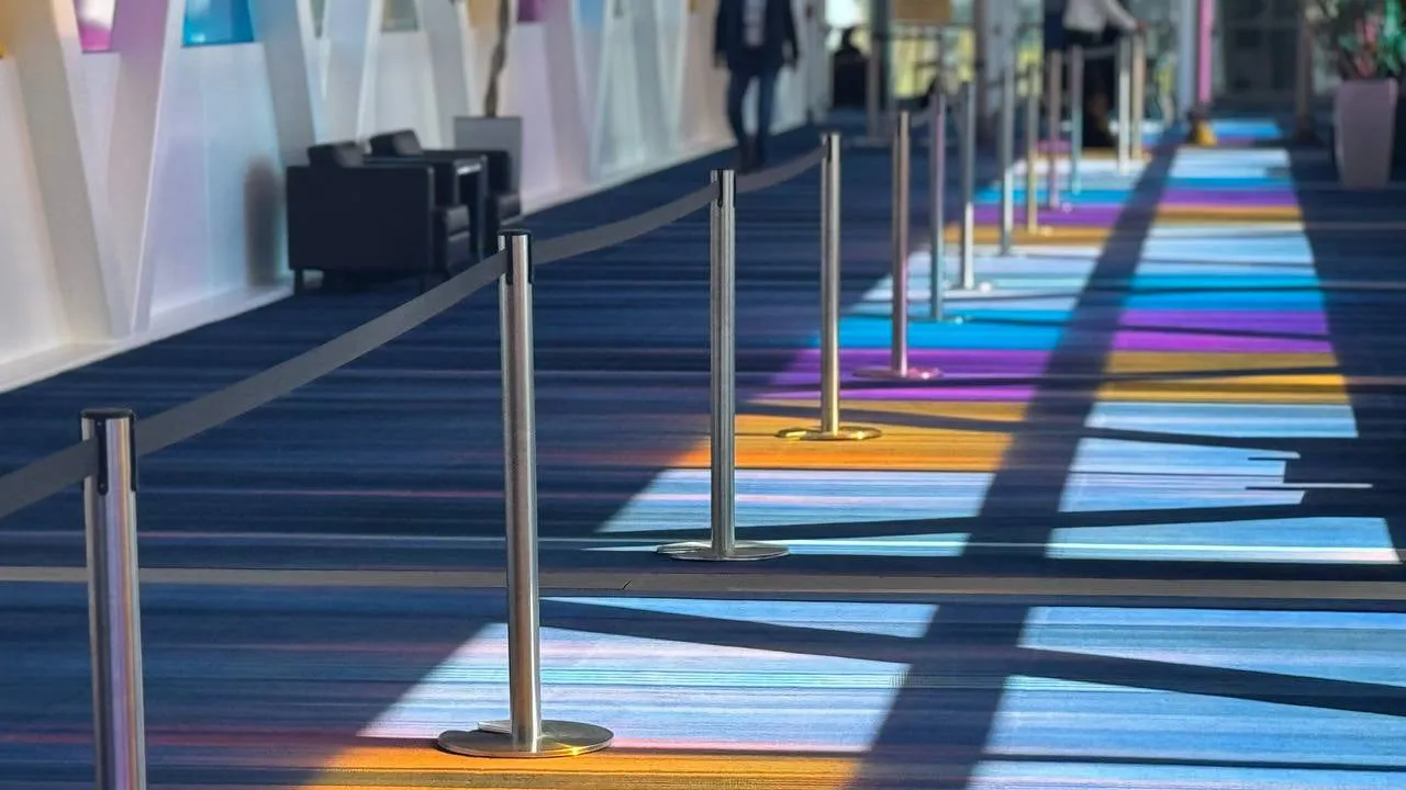 A row of silver stanchion posts down a lit convention centre concourse