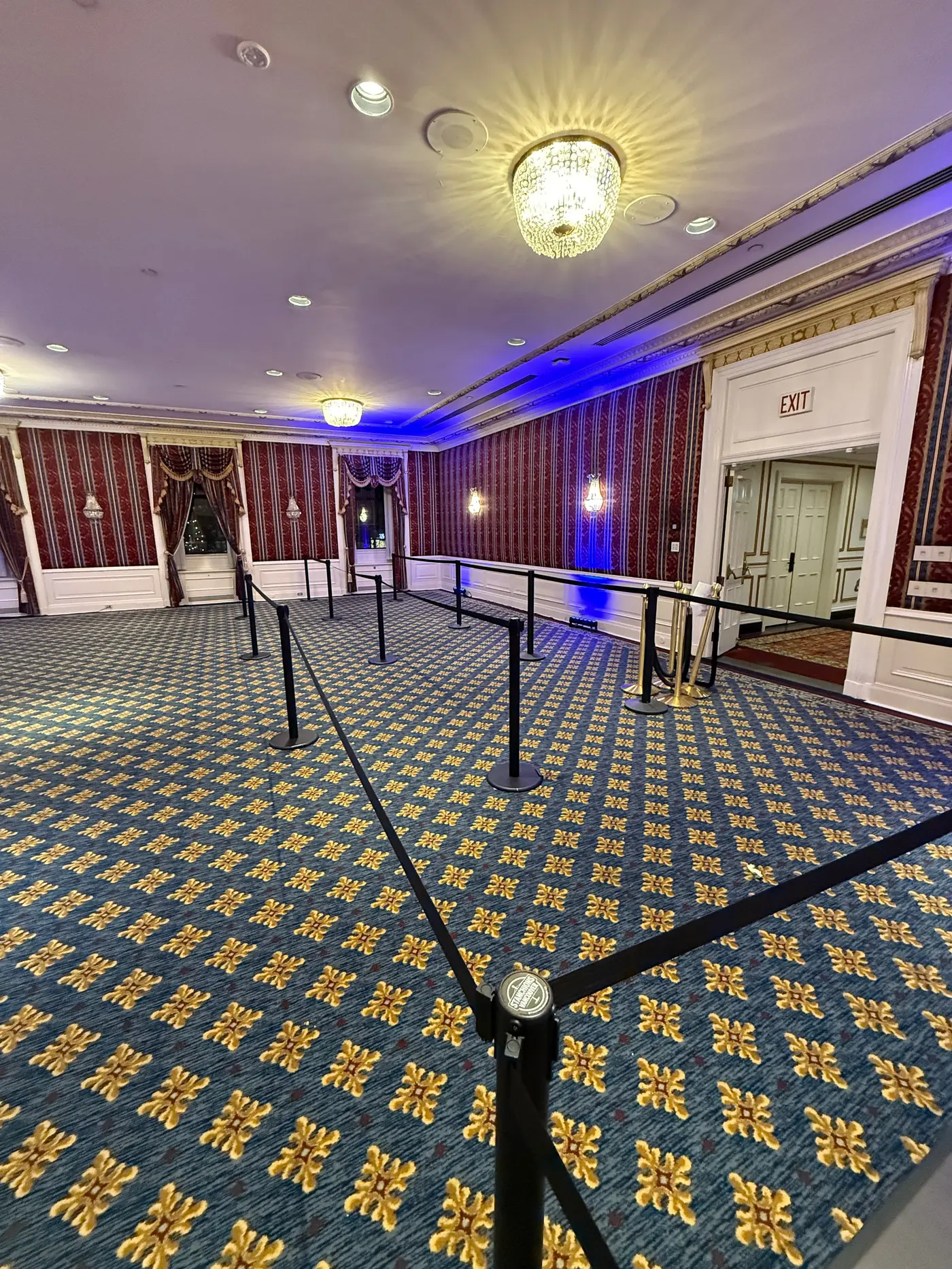 Belt stanchions set out as a queue across a patterned ballroom carpet