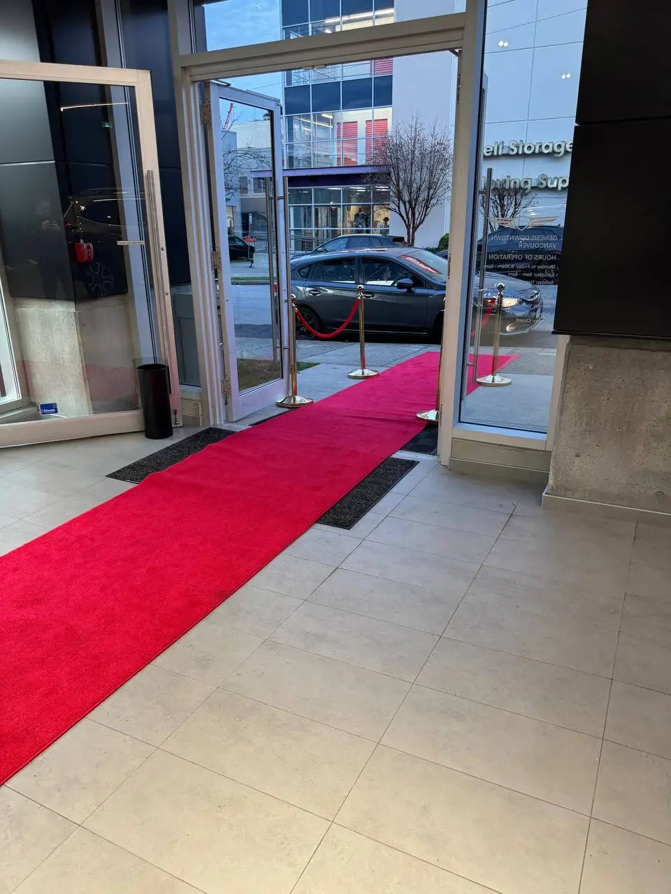 A red carpet runner leading in through glass entrance doors, a rope post at its edge