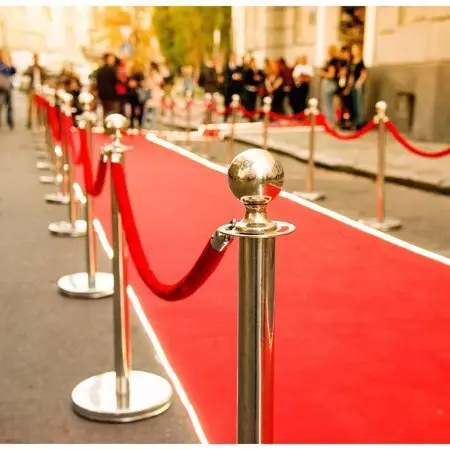Gold rope stanchions along a red carpet with a crowd standing behind them