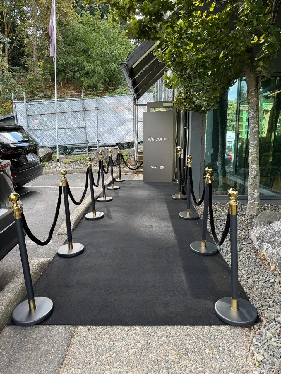 Black rope stanchions with gold tops and black velvet ropes lining a black carpet runner outdoors