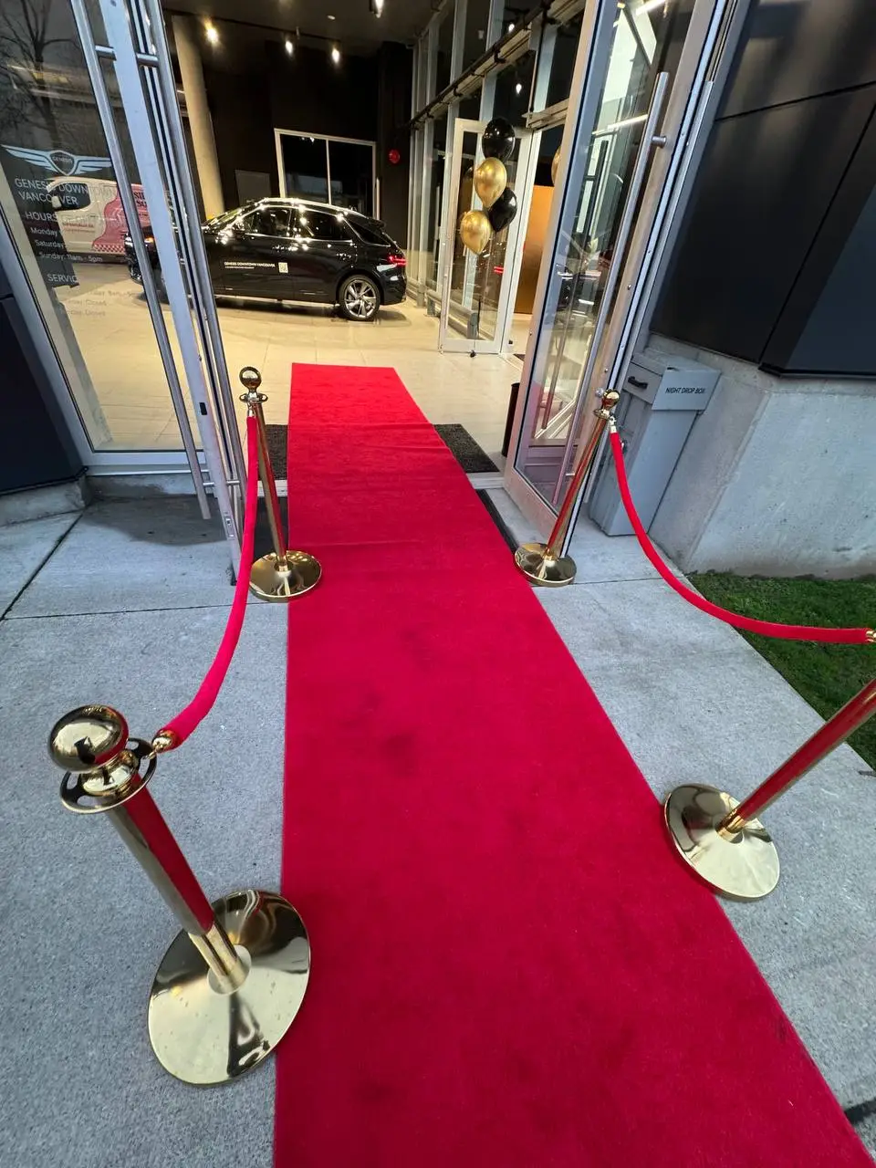Gold rope stanchions along a red carpet at a car showroom entrance