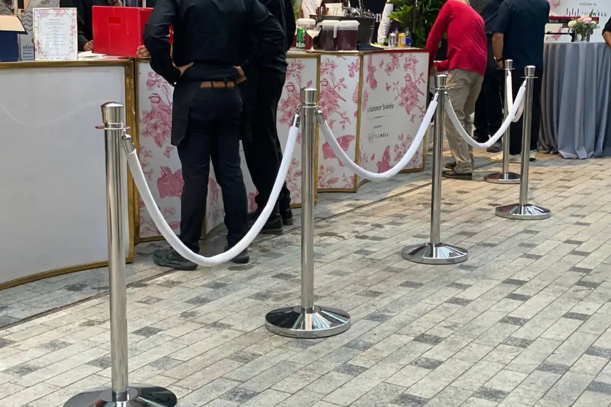 Cream velvet ropes on chrome posts holding a line at an outdoor reception