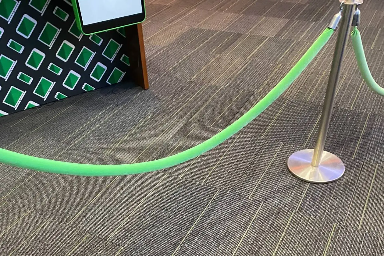 A bright green velvet rope hooked between chrome posts on grey carpet tiles