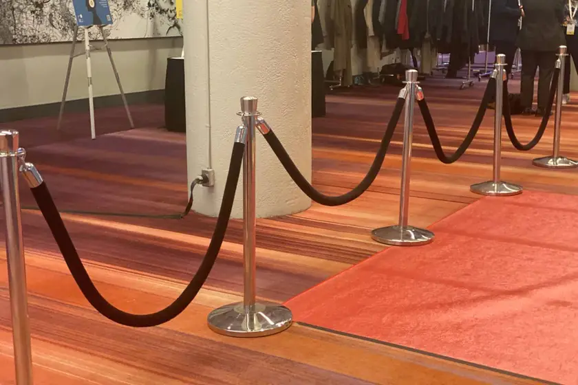 Black velvet ropes on chrome posts along a wooden floor beside a carpet runner
